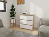A modern dresser with white drawers and a wood-effect top is placed in a room with two sofas and a potted plant. Náhled obrázku produktu