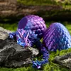 A crystal dragon toy and two dragon eggs are placed on rocks and moss. Produktbild-Vorschau