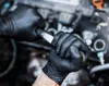 Hands wearing black nitrile gloves are using a wrench to work on a car engine. Náhľad obrázku produktu