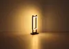 A modern lamp with a rectangular frame, lit from within, is placed on a flat surface against a plain wall. Produktbild-Vorschau