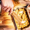 A hand is using tongs to pick up food from a metal container. Produktbild-Vorschau