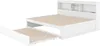 A white sofa bed with a pull-out trundle bed is shown against a white background. The sofa bed has a built-in bookshelf headboard. Náhled obrázku produktu