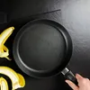 A frying pan with banana peels on a black surface. Produktbild-Vorschau