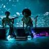 Two children sitting on a ledge in front of a large aquarium with glowing scooters. Voir les images du produit