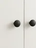 Two black round cabinet knobs are shown on a white cabinet door. Produktbild-Vorschau