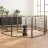 A black dog sits inside a metal playpen set up in a living room with plants and furniture in the background. Podgląd zdjęcia produktu