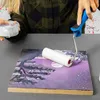 A person is painting a wooden board with a roller and a small container of paint. Produktbild-Vorschau