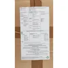 A piece of paper with instructions and information is taped to a cardboard box. Produktbild-Vorschau