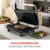 A close-up of a grill with a steak on it, with vegetables on a plate nearby. The background shows a kitchen setting. Produktbild-Vorschau