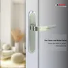A close-up of a silver door handle on a white door, with a blurred background of a room interior. Produktbild-Vorschau