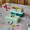 A children's lunchbox with food and marbles on a concrete surface with chalk drawings. Produktbild-Vorschau