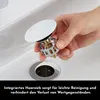 A hand is holding a sink drain stopper with an integrated hair strainer over a sink drain. Produktbild-Vorschau