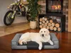 A golden retriever dog is lying on a dog bed in a living room with a motorcycle and a fireplace in the background. Náhled obrázku produktu