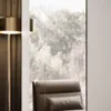 A close-up view of a modern armchair and a floor lamp, with a blurred background of trees visible through a window. Produktbild-Vorschau