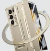 A gold-colored foldable phone case with a built-in stand, shown at an angle against a light gray background with a decorative gold ring around it. Náhled obrázku produktu