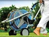 A person is using a hose reel cart on a grassy lawn with trees in the background. Podgląd zdjęcia produktu
