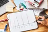 A desk with various office supplies, including a laptop, sticky notes, pencils, and a whiteboard with a graph being drawn on it. Voir les images du produit