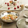 A festive table setting with a frying pan containing food, Christmas ornaments, and a lit candle. Anteprima dell’immagine prodotto