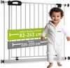 A baby in a white onesie stands next to a white safety gate with size indicators. Produktbild-Vorschau