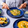 A person is eating a meal consisting of pasta, small tarts, and soup, served on blue plates. Voir les images du produit