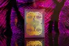 A deck of cards with a peacock design on a reflective surface with a colorful, abstract background. Produktbild-Vorschau