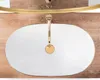 A top-down view of a white oval sink with a gold trim and a gold faucet, set against a wooden background. Anteprima dell’immagine prodotto