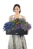 A woman is holding a planter filled with flowers. Produktbild-Vorschau