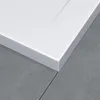 A close-up view of the corner of a white shower tray resting on a gray tiled floor. Produktbild-Vorschau