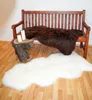 A wooden bench with two sheepskin rugs, one brown and one white, and two candles on a wooden stump. Produktbild-Vorschau