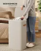 A person is putting laundry into a tall, beige laundry hamper in a bedroom. Produktbild-Vorschau