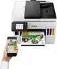 A Canon MAXIFY GX 7050 Multifunktionsdrucker is shown with a smartphone in hand, demonstrating its connectivity. Produktbild-Vorschau