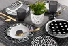 A table setting with black and white patterned dishes, gold cutlery, and a small potted plant. Produktbild-Vorschau
