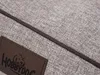A close-up view of a textured gray fabric with a brown leather tag and a dark cord detail. Produktbild-Vorschau