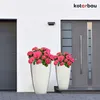 Two white ceramic planters with pink hydrangeas are placed on a paved walkway in front of a modern house with a gray door and a gray garage door. Náhľad obrázku produktu