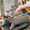 A person is grilling food on a portable gas grill outdoors. Produktbild-Vorschau