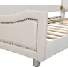 Close-up view of the side and headboard of a beige upholstered bed frame with silver nailhead trim. Náhled obrázku produktu
