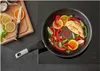 A frying pan with chicken and vegetables cooking on a stovetop, with a cutting board and knife nearby. Anteprima dell’immagine prodotto
