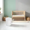 A white diaper pail is placed in front of a wooden crib in a nursery. Produktbild-Vorschau