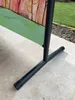 A close-up view of the base and lower part of a screen or divider, set up outdoors on a paved patio next to a grassy area. Produktbild-Vorschau