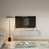 A modern living room with a TV mounted on the wall above a floating media console. A floor lamp stands to the left, and a coffee table with a book and pen is in the foreground. Voir les images du produit