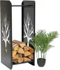 A black metal firewood rack with a tree silhouette design, filled with logs, stands next to a potted green plant. Podgląd zdjęcia produktu