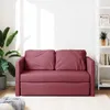 A red sofa bed is shown in a well-lit room with a plant on the left and a bookshelf on the right. Produktbild-Vorschau