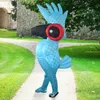 A person in a blue inflatable parrot costume walks on a paved path in a park with a stone building in the background. Produktbild-Vorschau