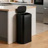 A black sensor trash can with its lid open, placed on a wooden floor next to a kitchen island. Podgląd zdjęcia produktu