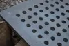A close-up of a cast iron grate with circular holes, resting on wooden planks. Voir les images du produit