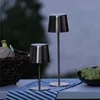 Two metallic table lamps are placed on a table with a striped cloth, next to a basket of items and a bowl of grapes. Podgląd zdjęcia produktu