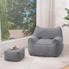 A gray beanbag chair and ottoman are placed in a living room setting with a large window overlooking trees and houses. Náhľad obrázku produktu