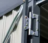 A close-up shot of a metal hinge on the side of a gray structure, with corrugated metal siding visible in the background. Podgląd zdjęcia produktu