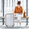 A woman sits on a bench at a transit station with a suitcase next to her. Anteprima dell’immagine prodotto