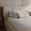 A close-up view of a bed with a textured headboard and pillows. Produktbild-Vorschau